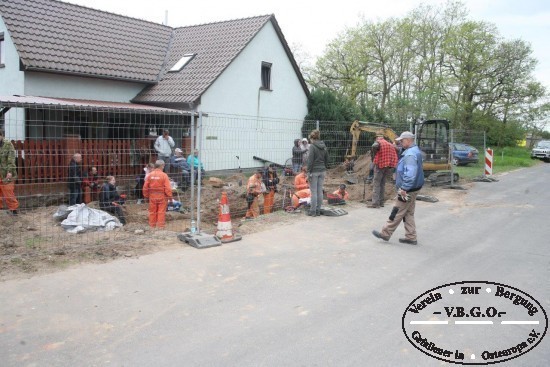 Eine Grablage ist vor dem Haus lokalisiert. Ein Bauzaun sichert die Grabungsstelle.